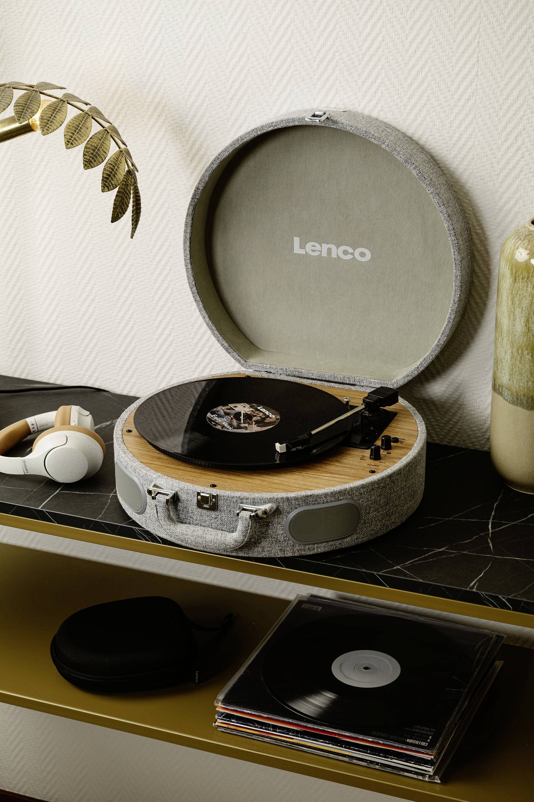 Otevřený gramofon s deskou stojí na poličce, vedle něj leží sluchátka. V pozadí je vidět rostlinu.