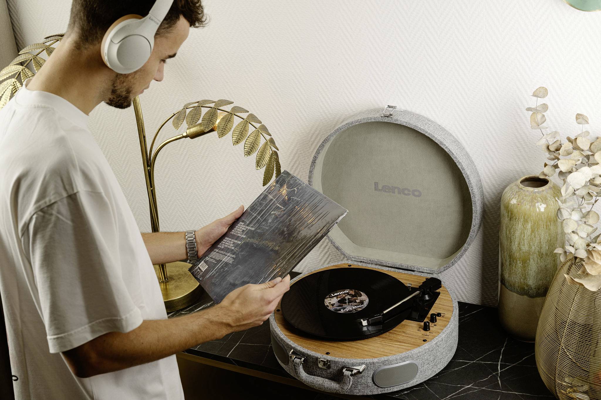 Muž se sluchátky pozoruje vinylovou desku vedle gramofonu v moderně zařízeném prostoru.