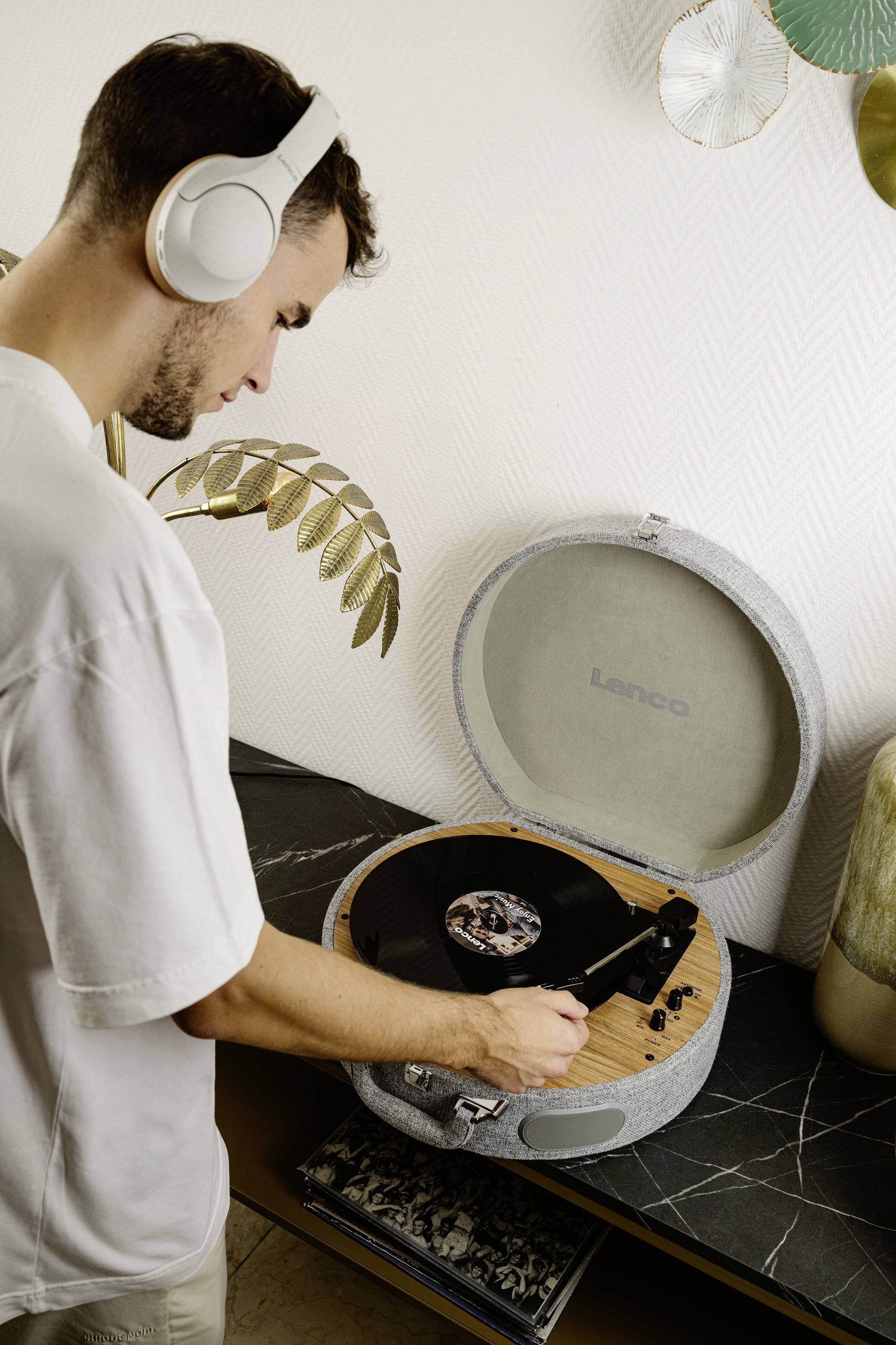 Muž se sluchátky pokládá gramofonovou desku na gramofon v moderním prostoru.