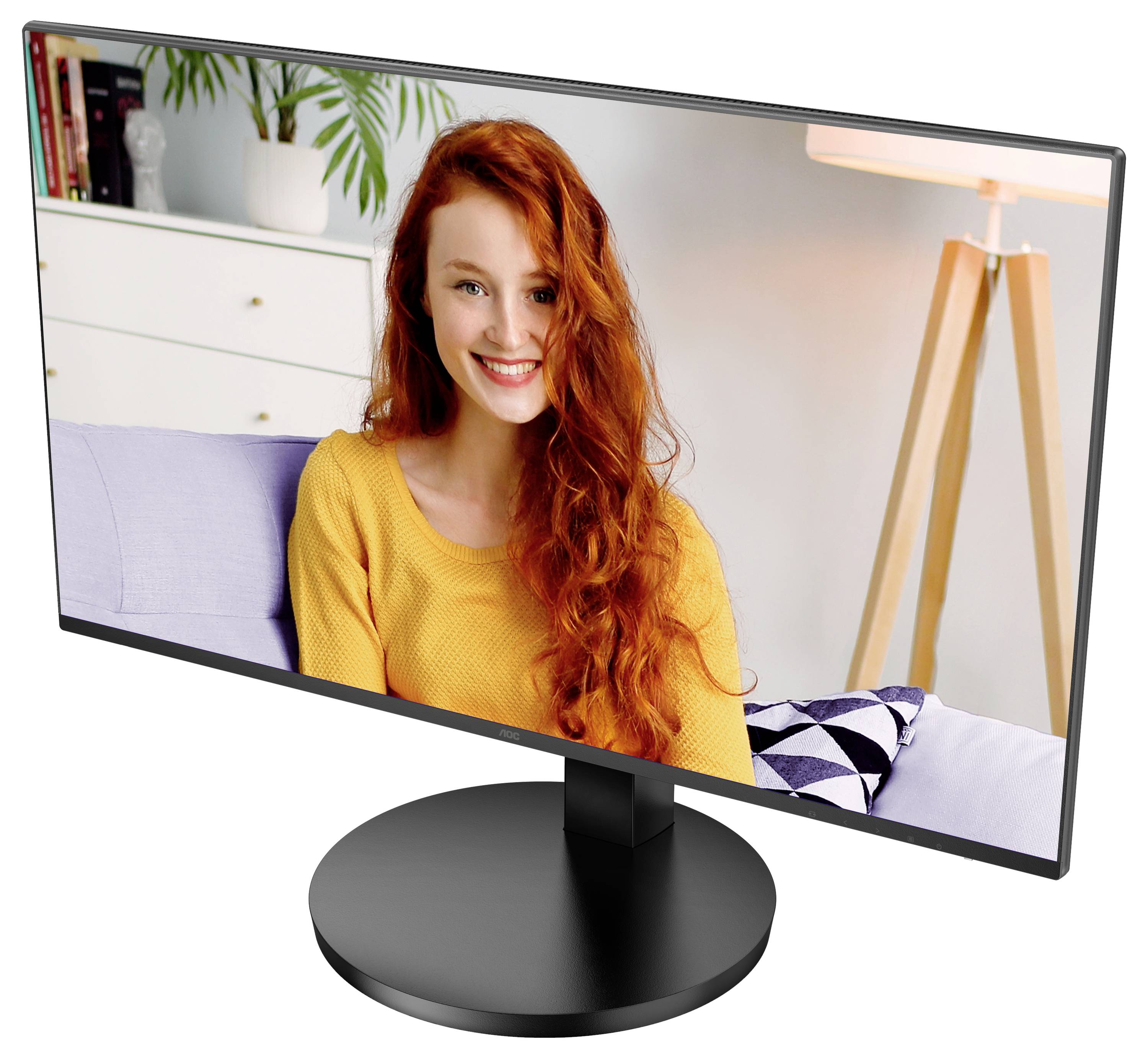 Žena s dlouhými rudými vlasy a žlutým svetrem se usmívá na obrazovce monitoru. V pozadí knihovna a stojací lampa.