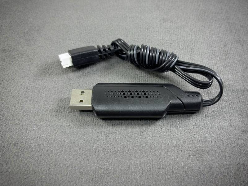 Černý USB kabel s obdélníkovým konektorem na jedné straně a kulatou zástrčkou na straně druhé, umístěný na šedém pozadí.