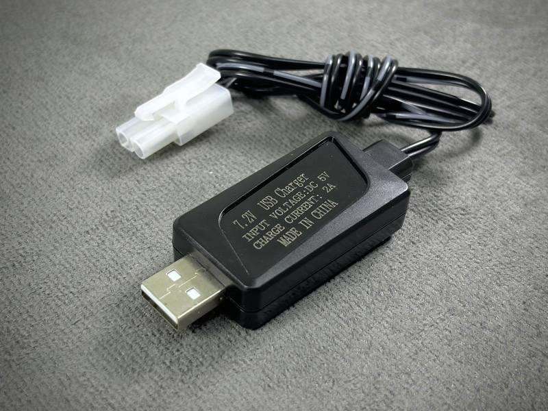 USB datový kabel s pravoúhlým adaptérem, ležící na koberci. Adaptér má nápis s informacemi o nabíjecím výkonu a zemi původu.