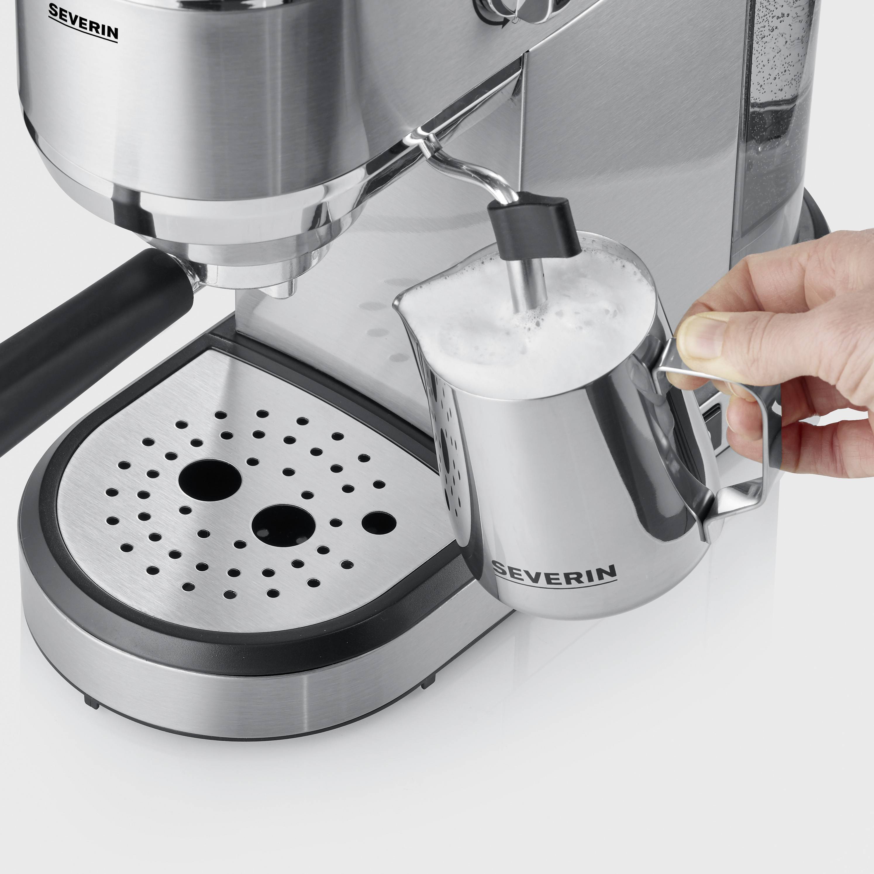Espresso machine with milk frother. A hand holds a small jug with frothed milk under the nozzle. Device made of stainless steel.