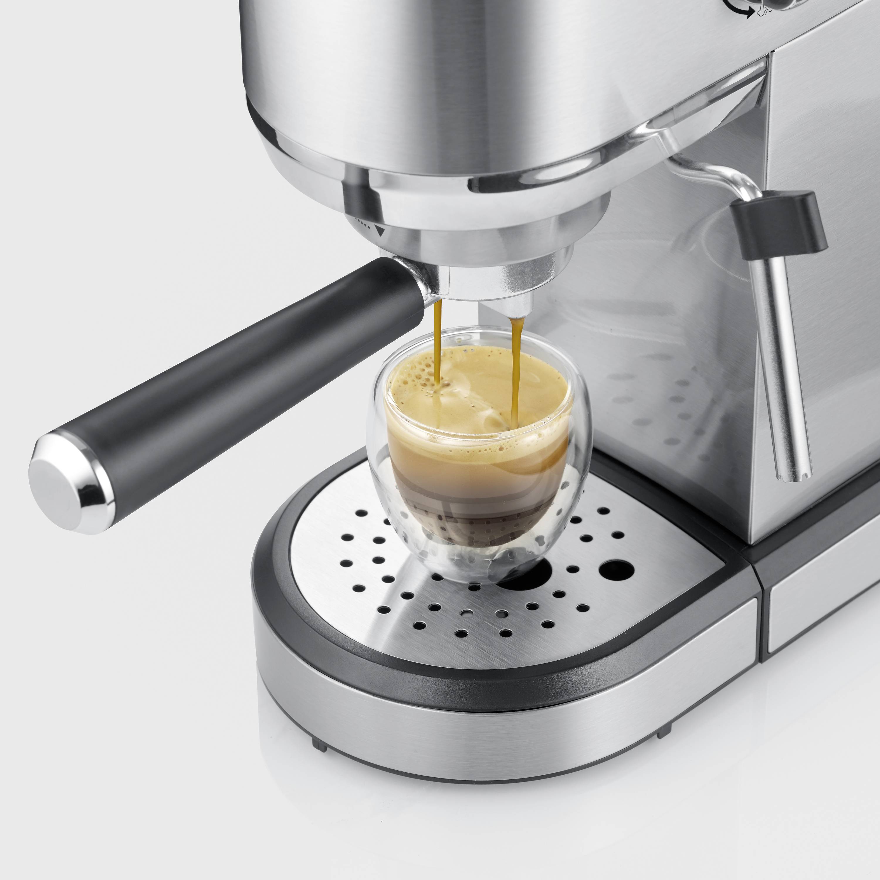 Espresso kávovar připravuje čerstvé espresso ve skleněné konvici, stříbrný design s parní tryskou. Káva vytéká z dvojitého výtoku.