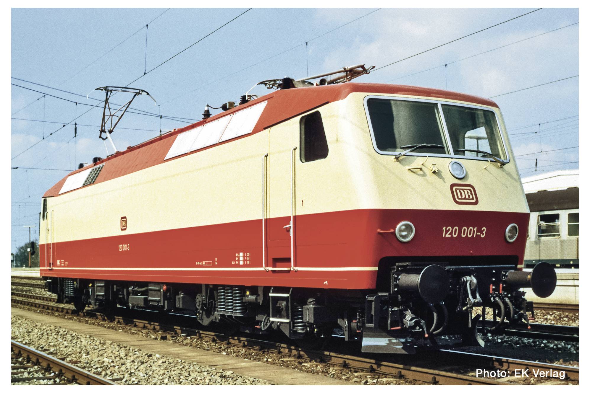 Červený a béžový elektrický vlak Deutsche Bahn stojí na kolejích za slunečného dne. V pozadí jsou viditelné další železniční koleje.