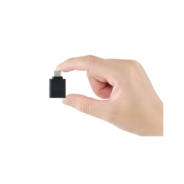 Jedna ruka drží malý černý USB adaptér s USB-C konektorem.