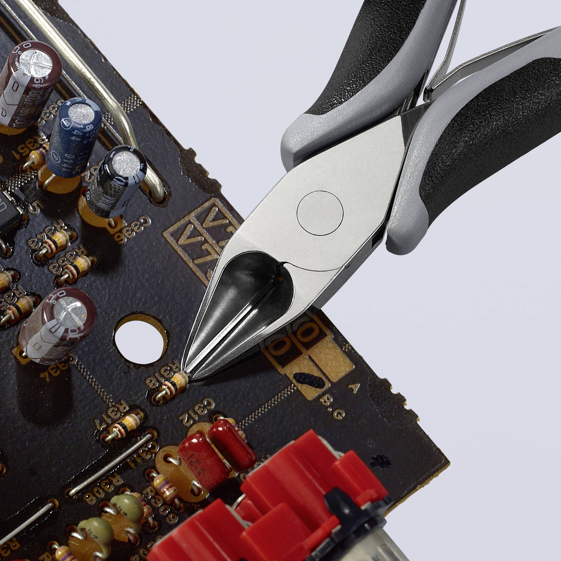 Detail elektronické desky plošných spojů s kondenzátory a komponenty, vedle kterých leží úhlopříčné štípací kleště, které lze použít pro elektrotechnické práce.