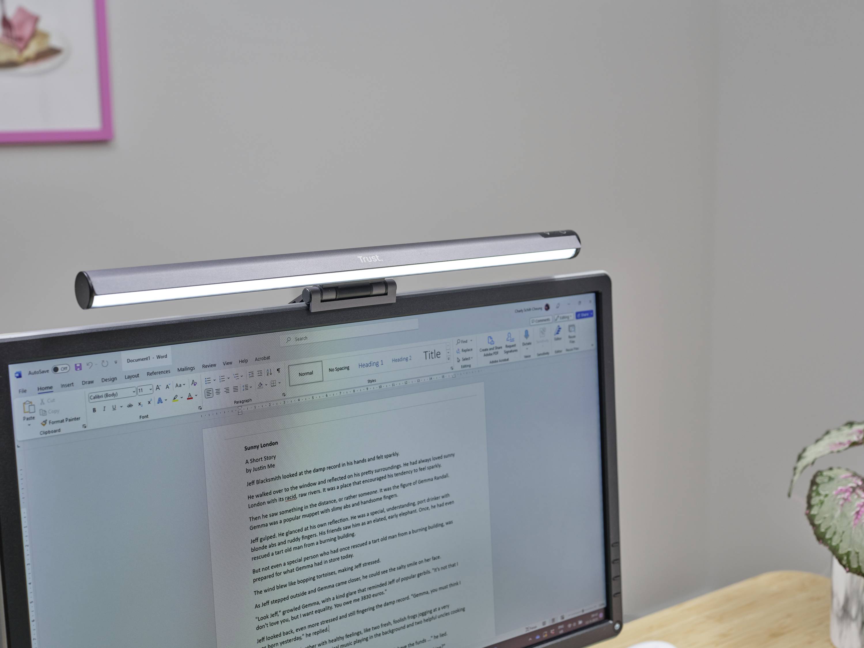 Stolní lampa je připevněna nahoře k monitoru, který zobrazuje textový dokument. Pozadí je rozmazané s detailními prvky.