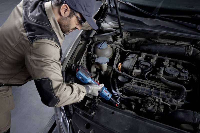 Mechanik pracuje s diagnostickým zařízením na motoru automobilu v autoservisu, má na sobě ochranný oděv a ochranné brýle.