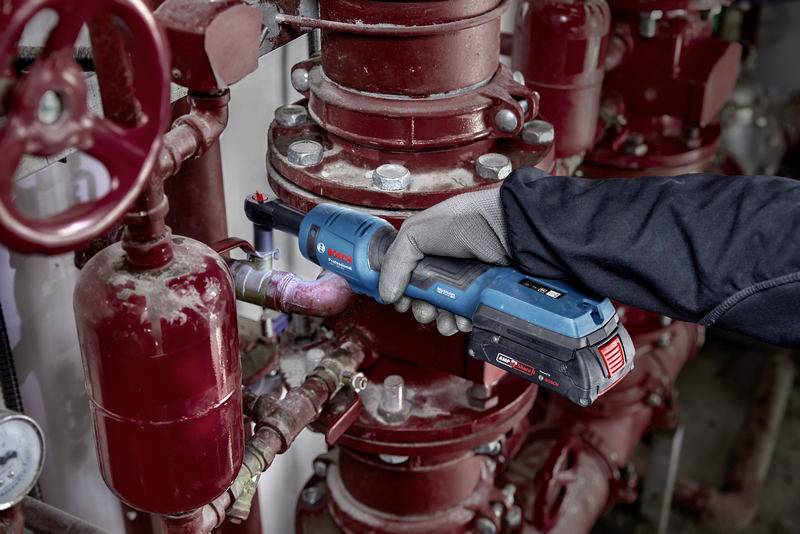 Osoba pracuje s modrým elektrickým nástrojem na červeném potrubním systému.