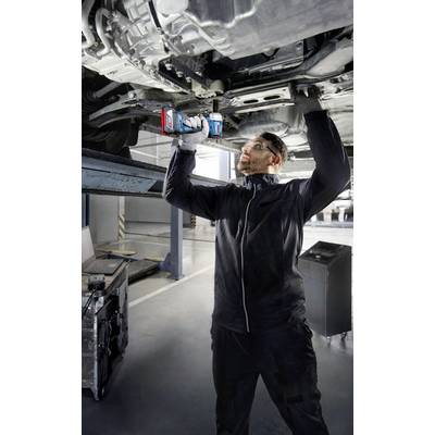 Mechanik pracuje s elektrickým nástrojem na spodní straně zvednutého vozidla v prostředí autodílny.