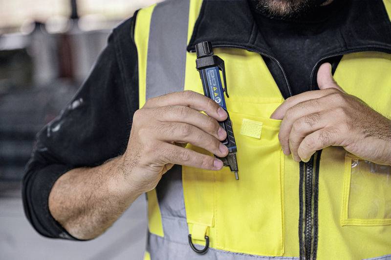 Osoba v žluté pracovní vestě si zasouvá modrý fix do náprsní kapsy. V pozadí je pracovní prostředí.