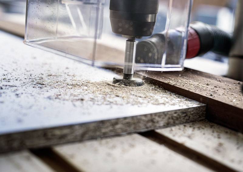 CNC stroj frézuje přesné linie do dřevěné desky, obklopené pilinami.