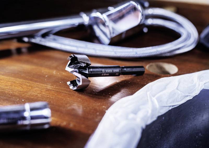 Detailní záběr 28mm vrtáku na dřevěném stole, obklopeného ohebnou kovovou trubkou a chromovaným nástrojem.