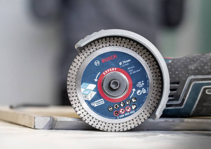 Úhlová bruska s diamantovým kotoučem, označená logy a specifikacemi, leží na pracovním stole.