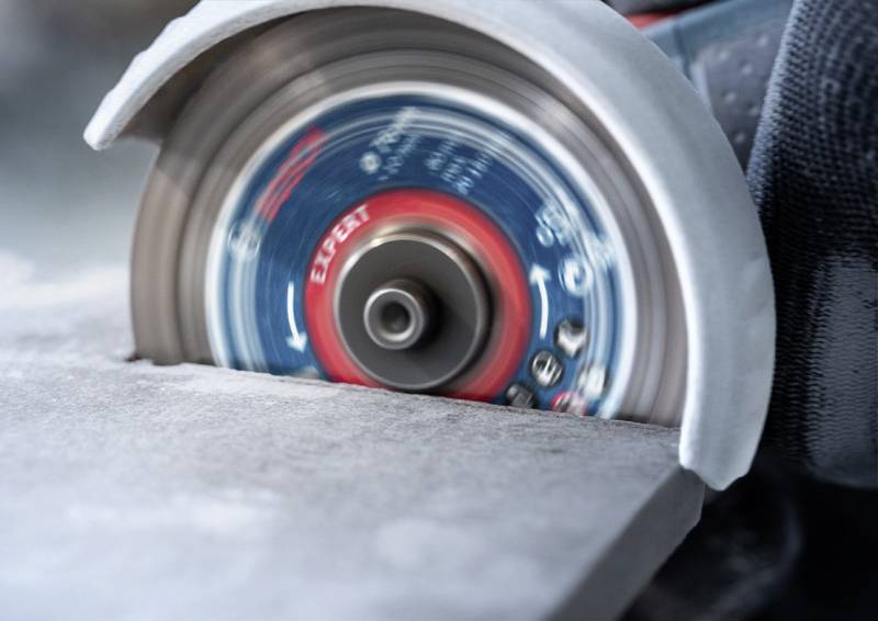 Kotoučová pila přesně řeže kamennou desku. Rotující kotouč je v pohybu a vytváří jemný prach.