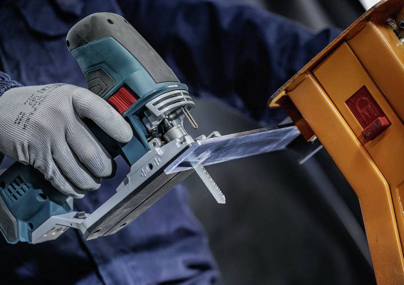Řemeslník řeže pomocí elektrické přímočaré pily dřevěný kus. Scéna ukazuje bezpečnost práce s použitím rukavic.
