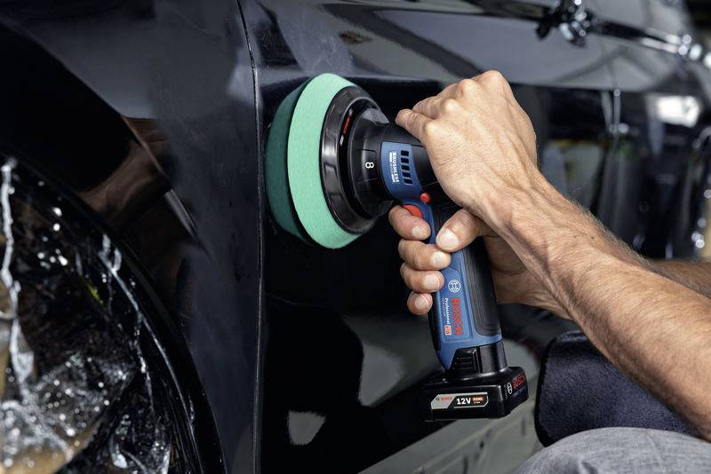 Osoba leští lak černého automobilu elektrickou leštičkou. Díky ošetření auto získává lesk.