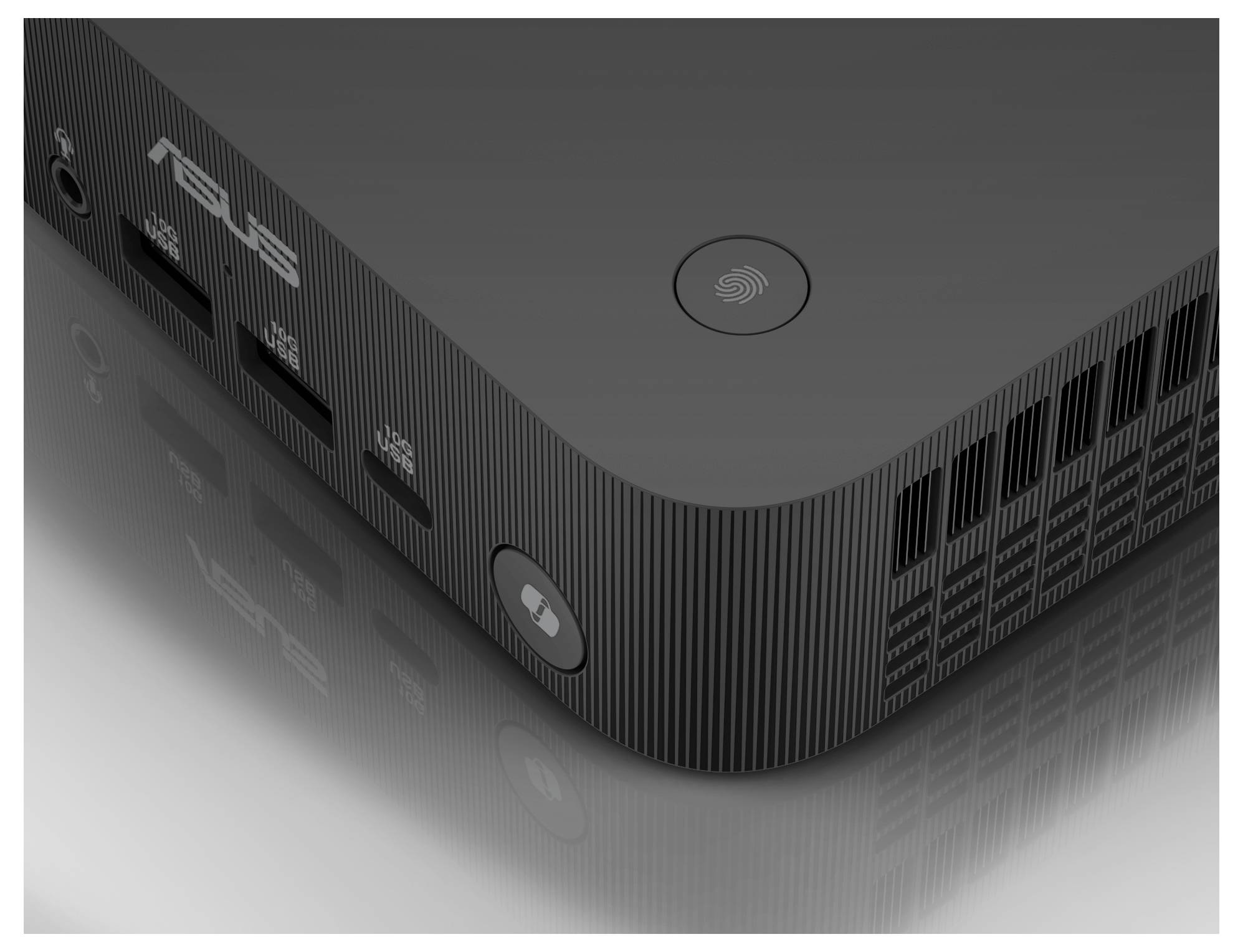Černý miniaturní počítač ASUS s firemním logem, USB porty a větracími otvory, umístěný na reflexní ploše.