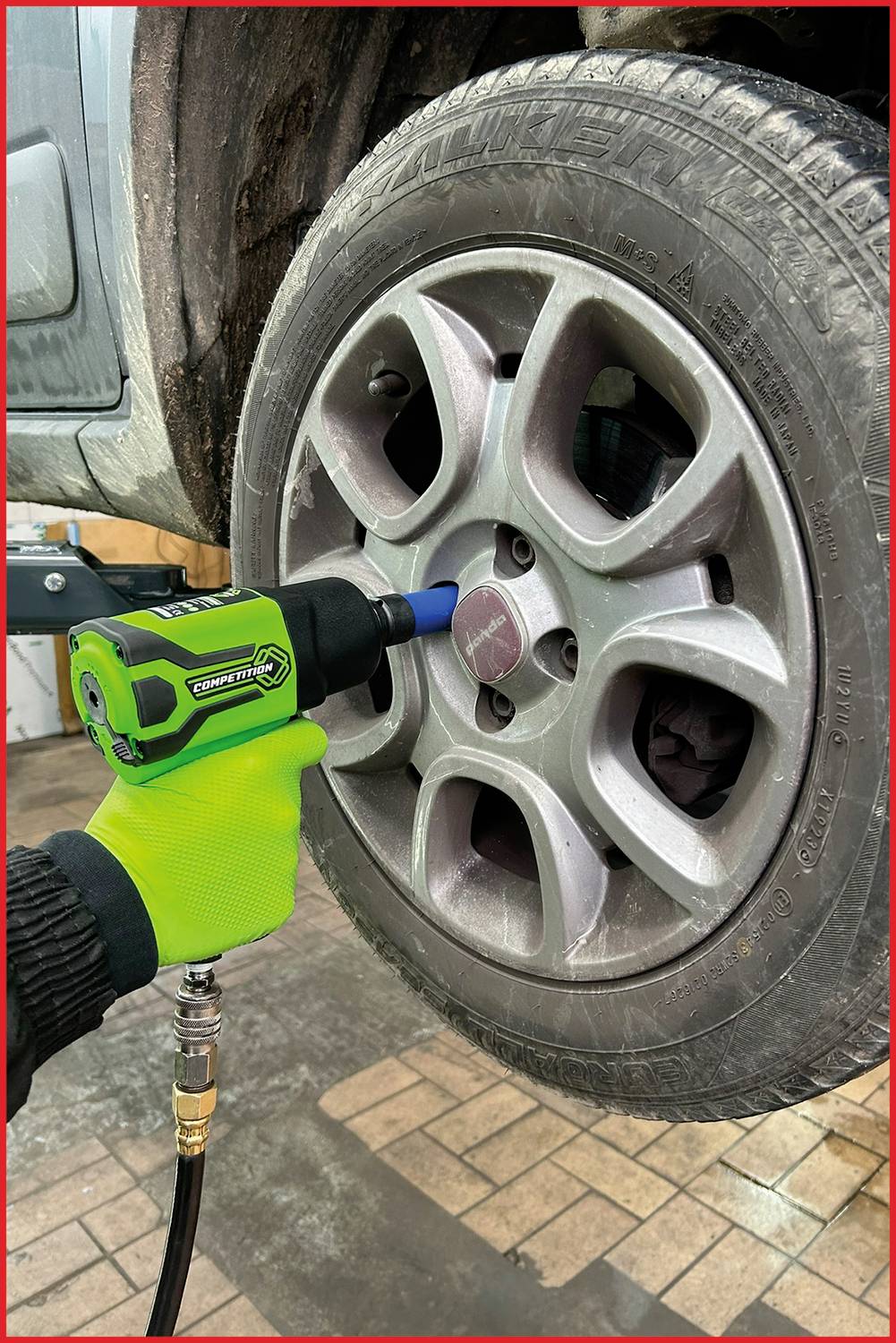 Osoba používá zelený rázový utahovák k upevnění šroubů kola černého pneumatiky v dílně.