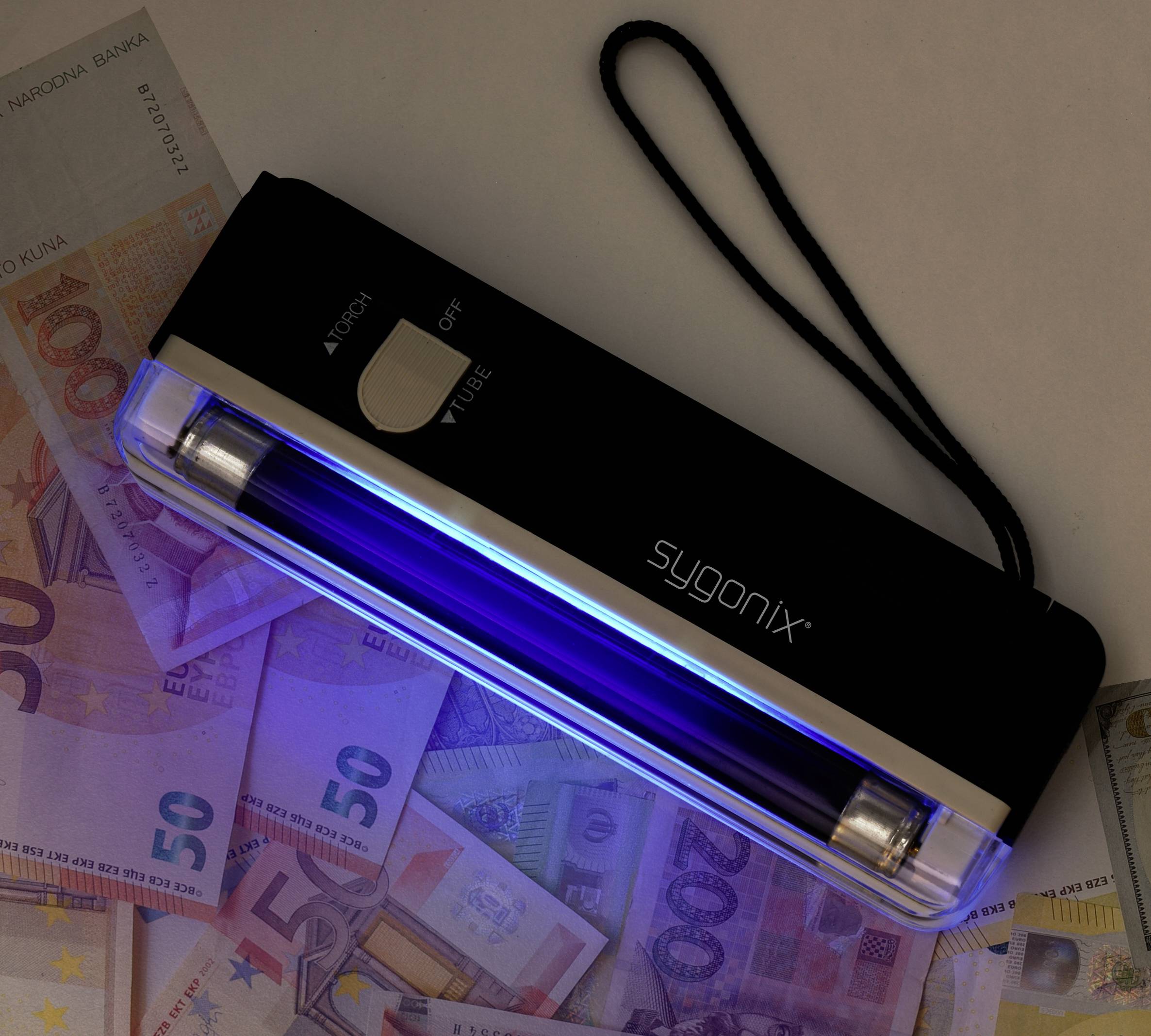 Ruční UV detektor padělků se zářícím modrým světlem leží na několika eurobankovkách a odhaluje bezpečnostní prvky měny.