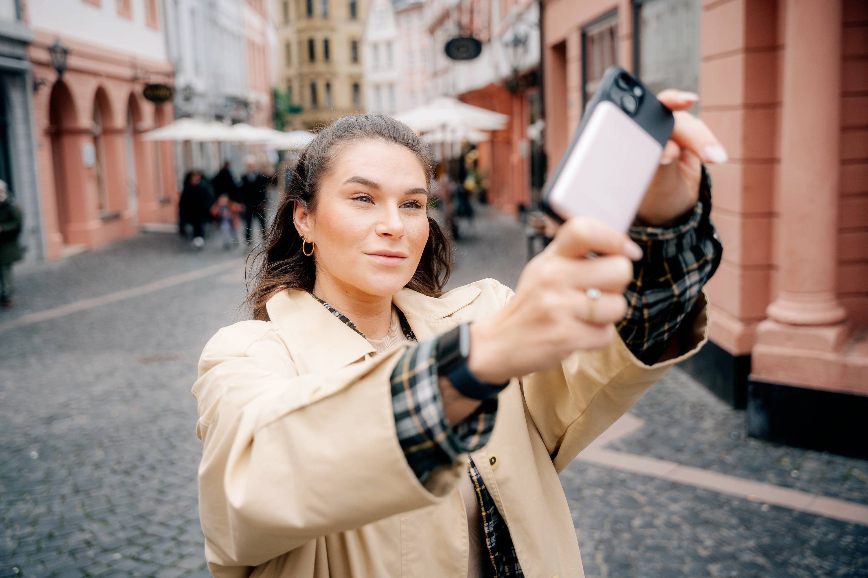 Žena si pořizuje selfie na dlážděné ulici ve staré části města s barevnými budovami v pozadí.