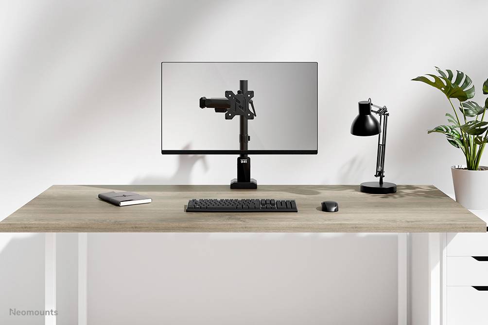 Moderní psací stůl s monitorem, klávesnicí, myší, lampou, poznámkovým blokem a rostlinou. Minimalistický design.