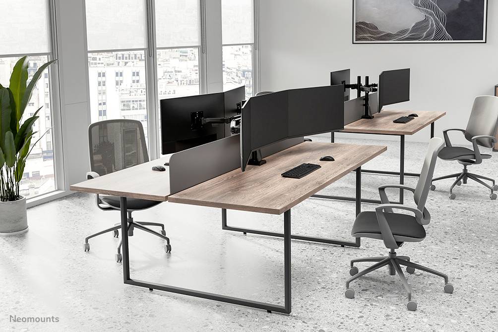 Moderní kancelářské prostory s několika pracovními stoly a monitory, ergonomické židle. Velká okna s výhledem na město v pozadí.