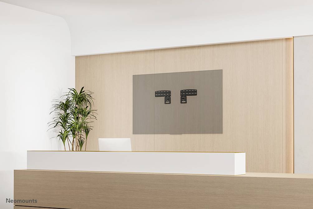 Moderní recepční pult vyrobený z dřeva, s květináčem vlevo a nástěnným držákem na obrazovku na stěně v pozadí.