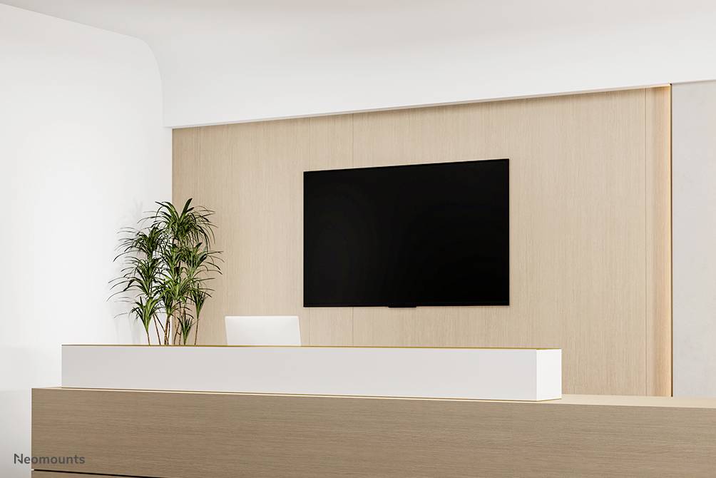 Recepční pult v moderní kanceláři, s rostlinou nalevo a velkým nástěnným monitorem nad pultem.