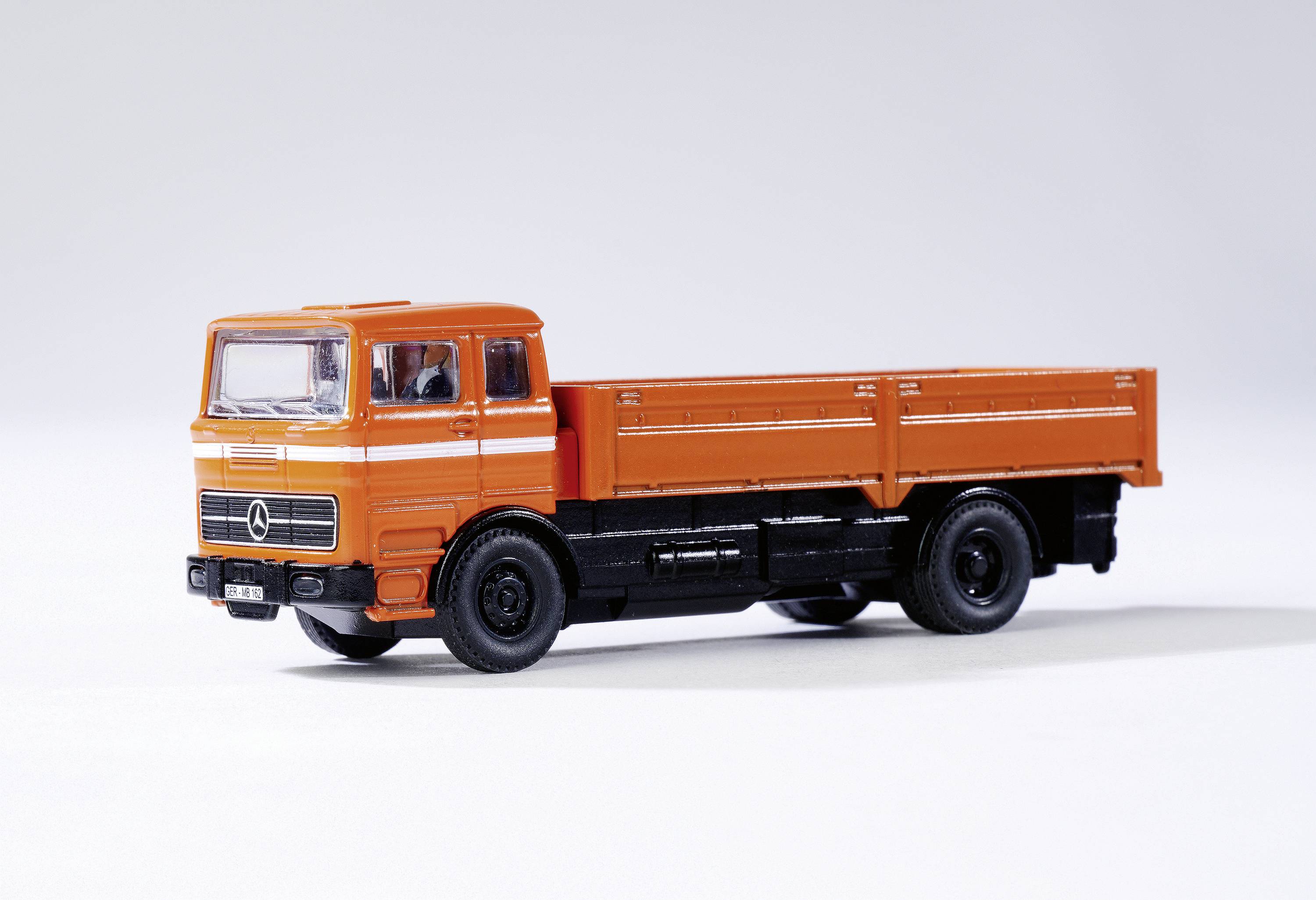 Oranžový model nákladního vozu klasického designu na bílém pozadí. Nákladní vůz má otevřenou ložnou plochu bez nákladu.