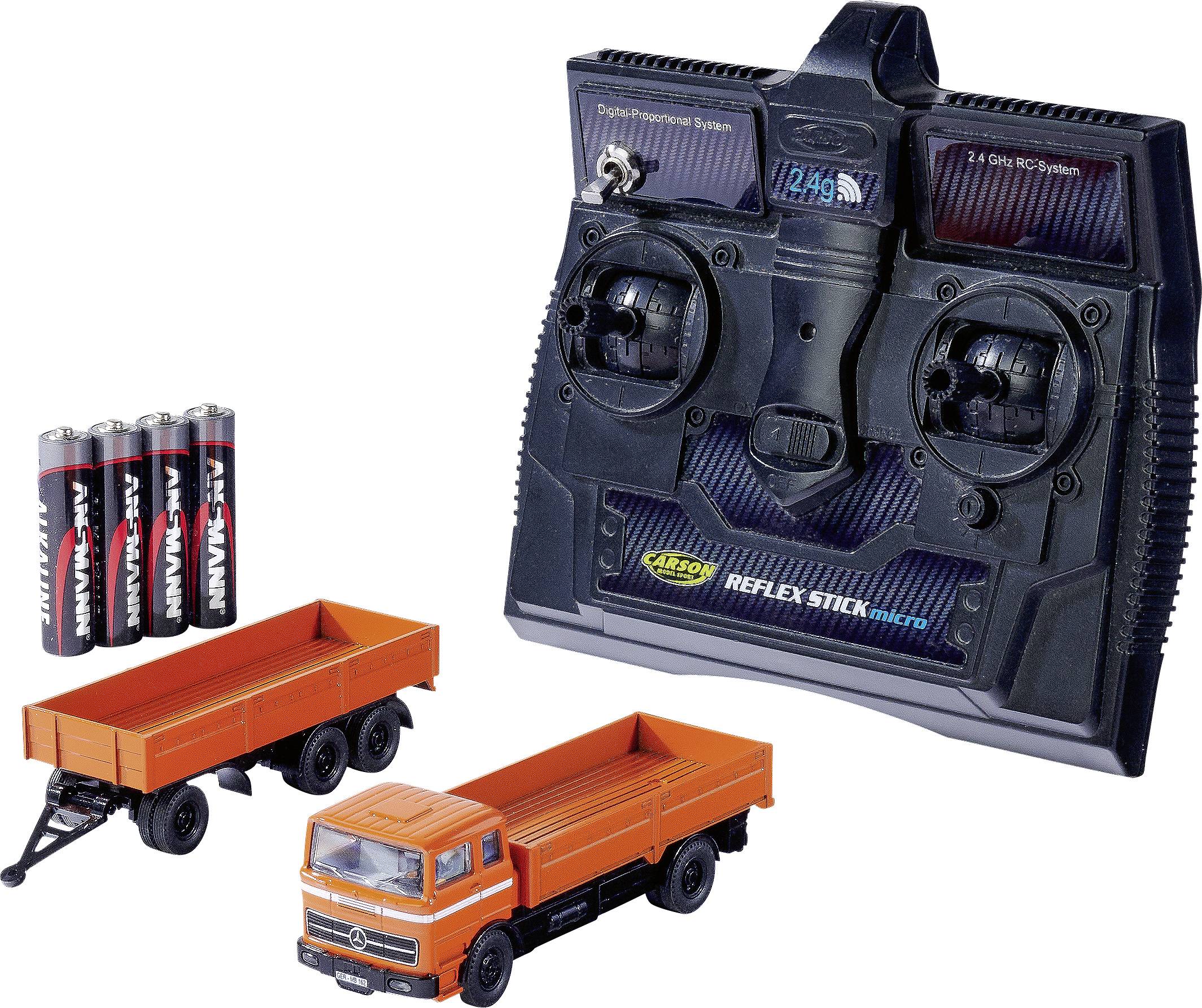 Rádiové ovládání pro RC vozidla, typ 'CARSON Reflex Stick Micro' vedle hračky nákladního automobilu a baterií.