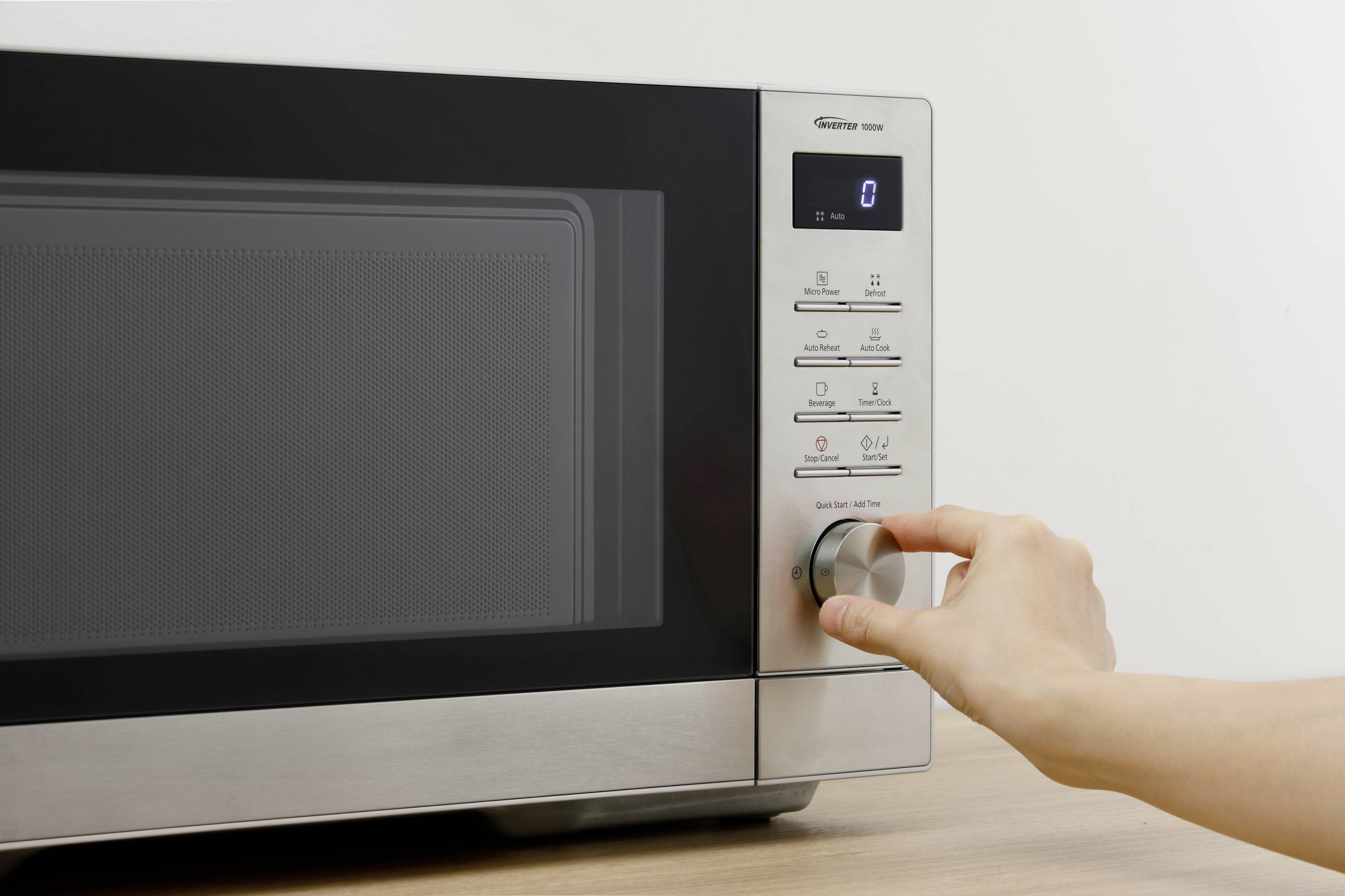 Ruka otáčí ovladačem moderní mikrovlnné trouby. Displej zobrazuje čas. Pravoúhlý design, povrch z nerezové oceli.