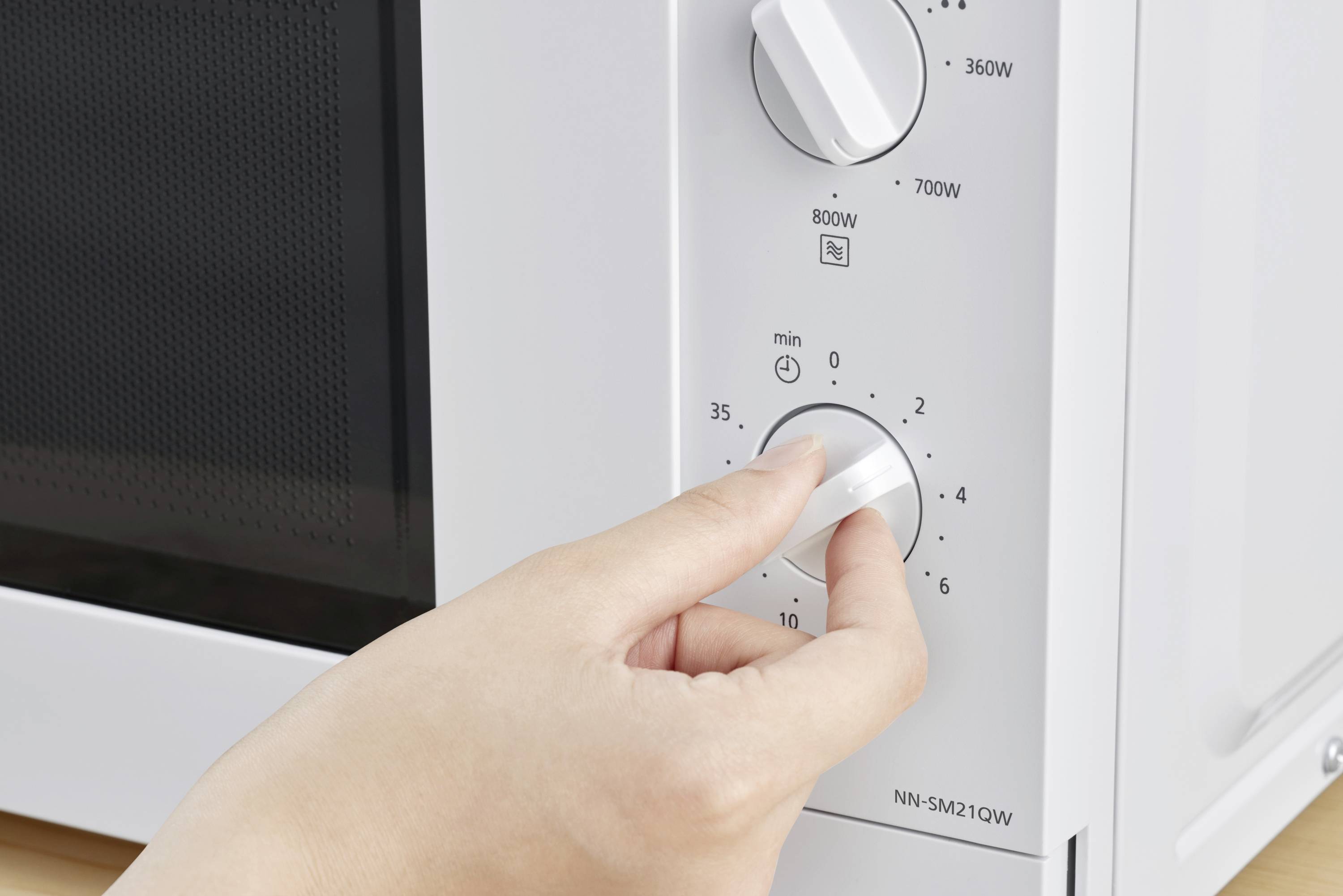 Ruka otáčí časovačem mikrovlnné trouby, aby nastavila dobu vaření. Výkonové stupně jsou označeny 360W, 700W a 800W.