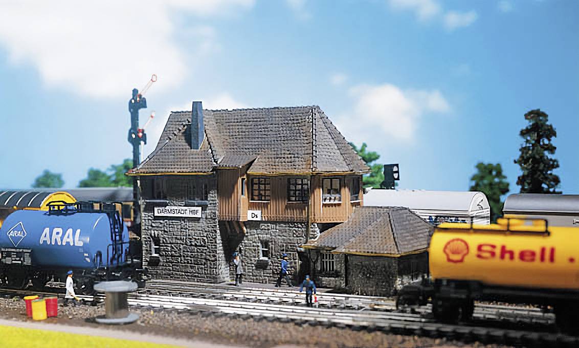 Miniaturní nádraží s betonovým objektem a dvěma modelovými kolejemi. Vlevo vlak s logem 'ARAL', vpravo vlak s logem 'Shell'.
