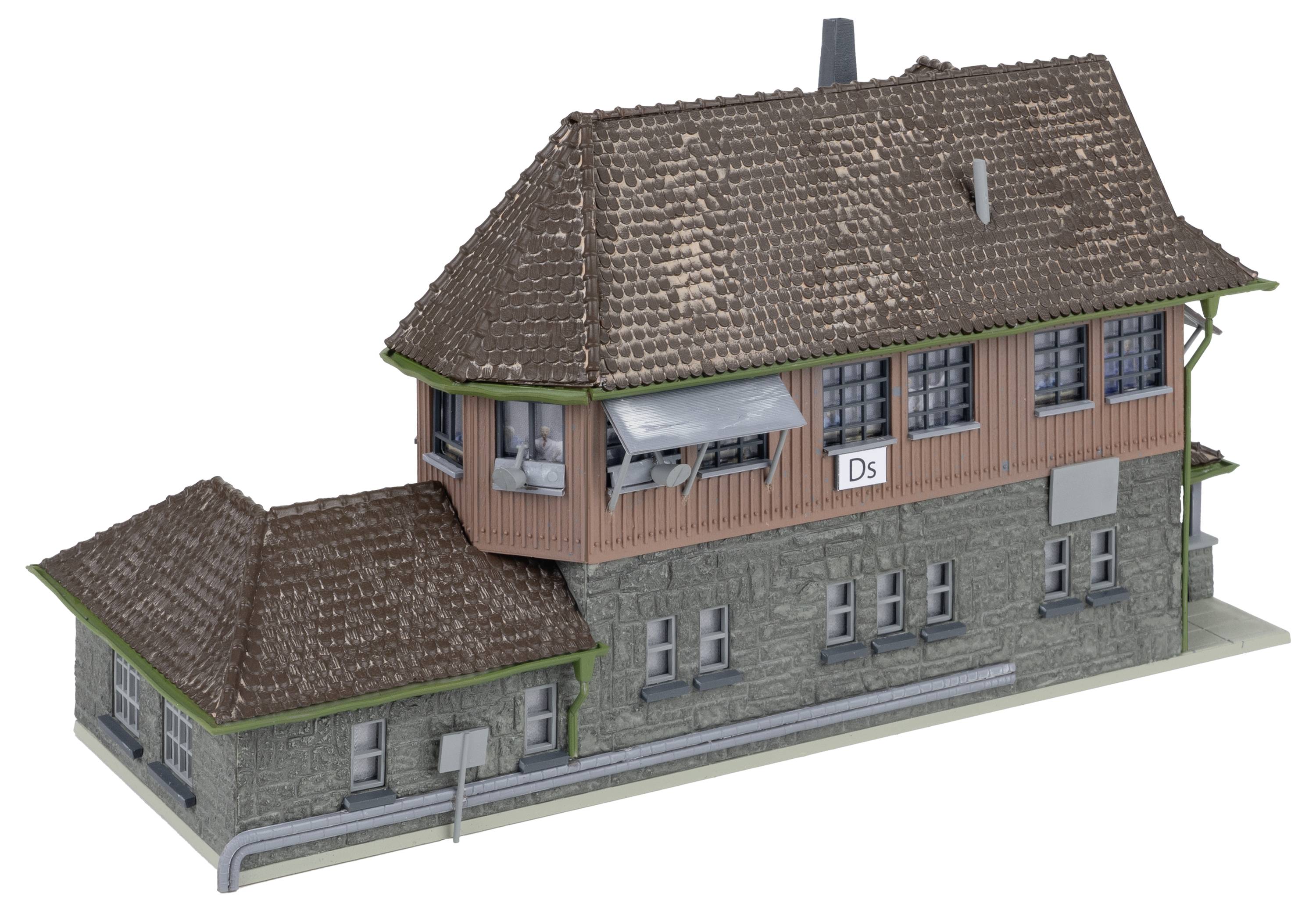 Model starého nádražní budovy s cihlovou střechou a cedulkou s nápisem 'Ds'. Budova ve stylu hrázděné architektury.