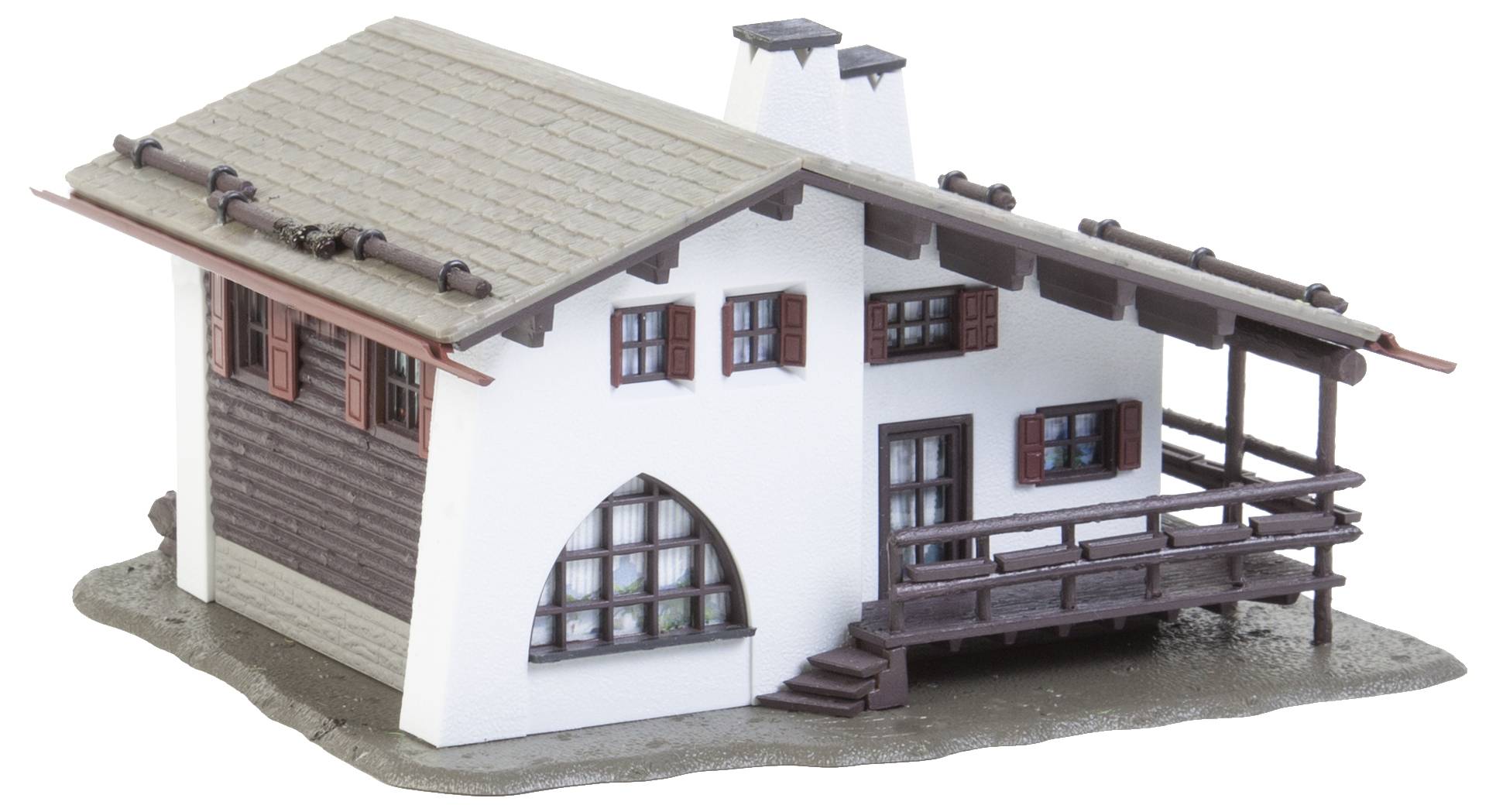 Malý model alpského domu se dřevěnou verandou a komínem. Bílá omítka a hnědé dřevěné prvky na šedém podstavci.