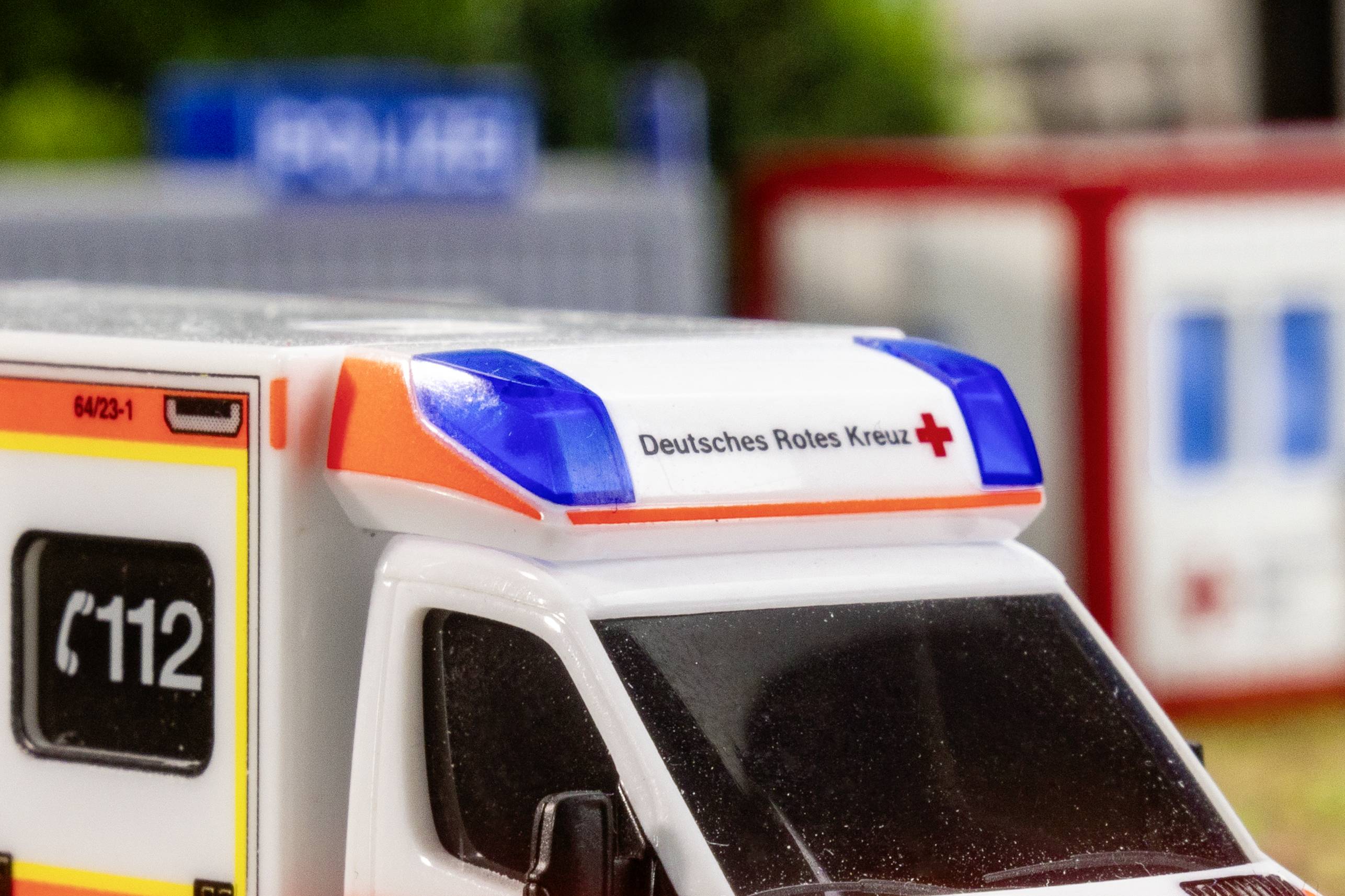 Sanitní vůz Německého červeného kříže s tísňovou linkou 112 na boku. V pozadí rozmazané budovy.