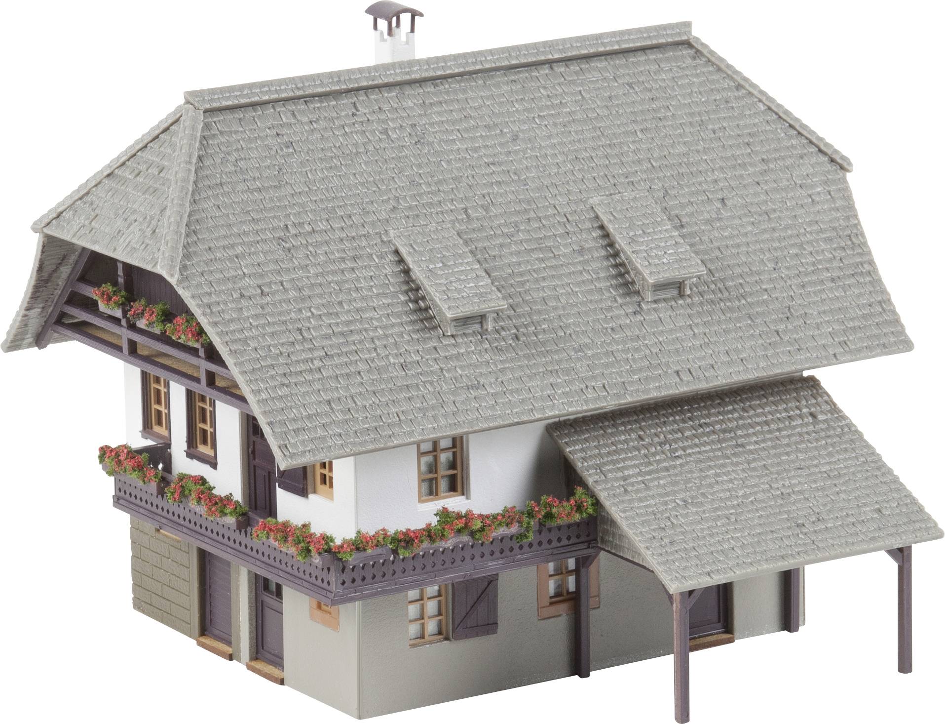 Miniaturní model tradičního selského domu se šedou šindelovou střechou, balkónem a truhlíky s červenými květinami.