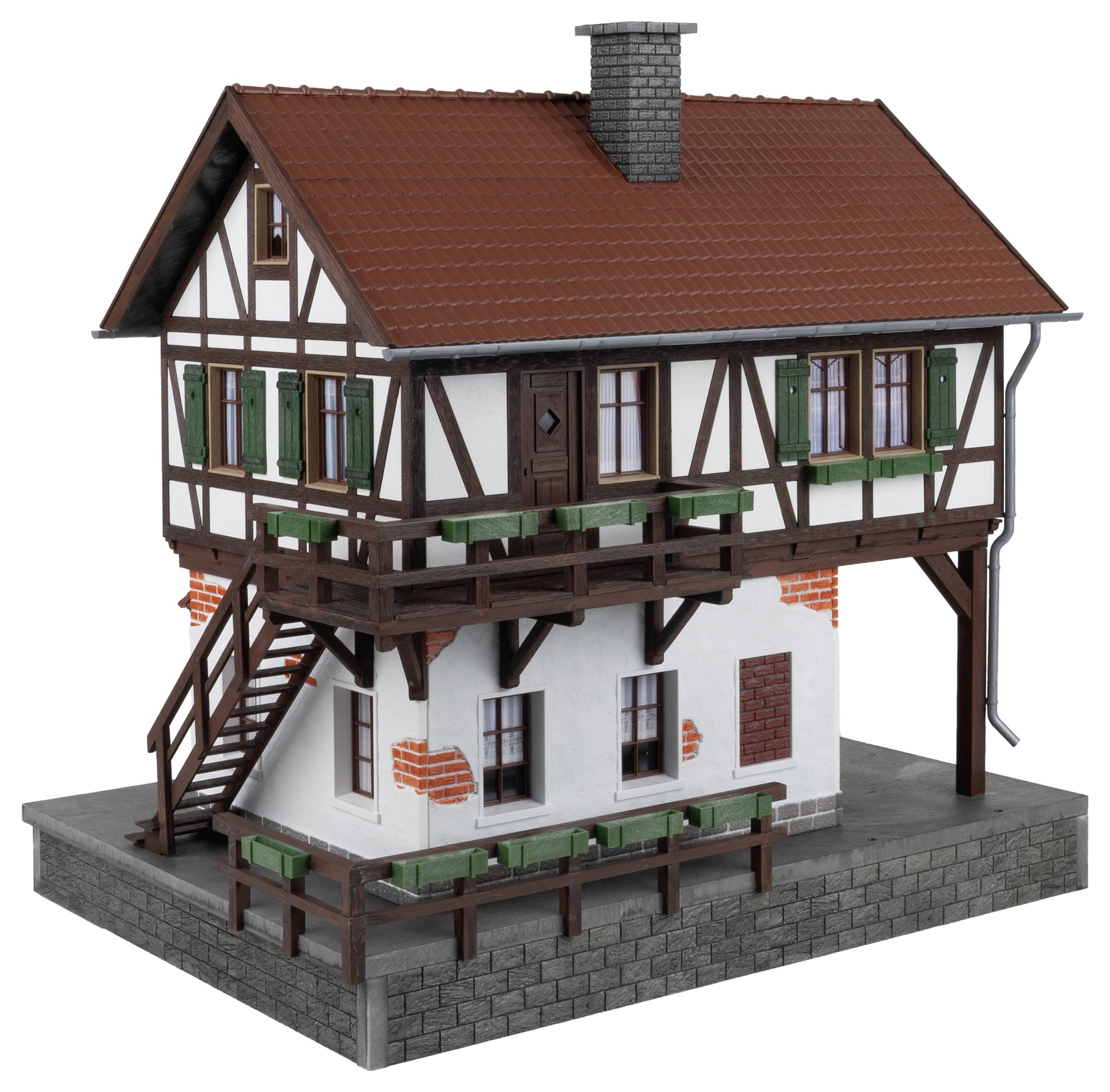 Detailní model hrázděného domu na podstavci, se střechou z červených tašek, zelenými okenicemi a viditelnými cihlářskými strukturami.