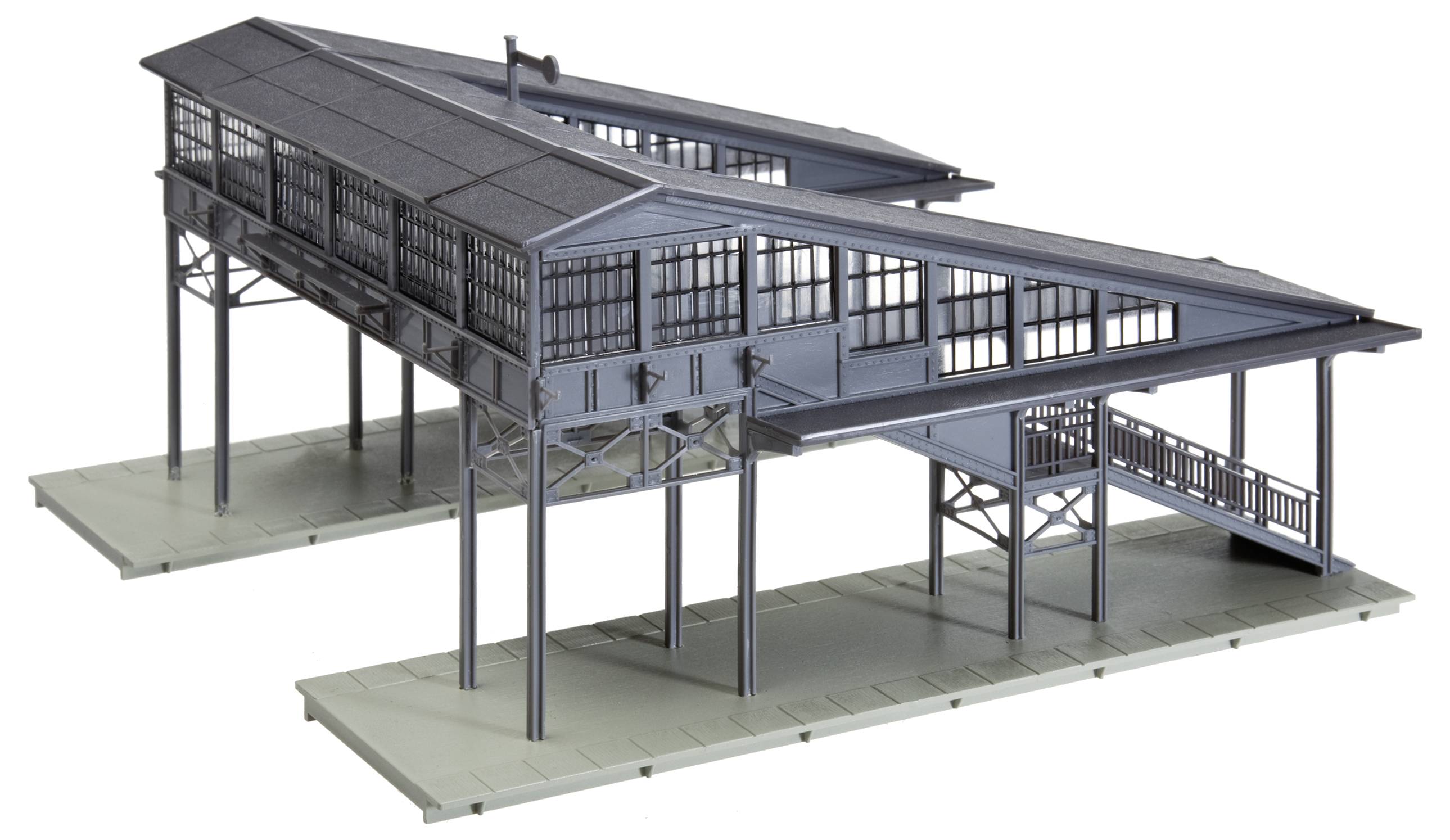 Model moderního nádražního objektu s velkými prosklenými okny umístěný na zvýšené struktuře nesené kovovými podpěrami.