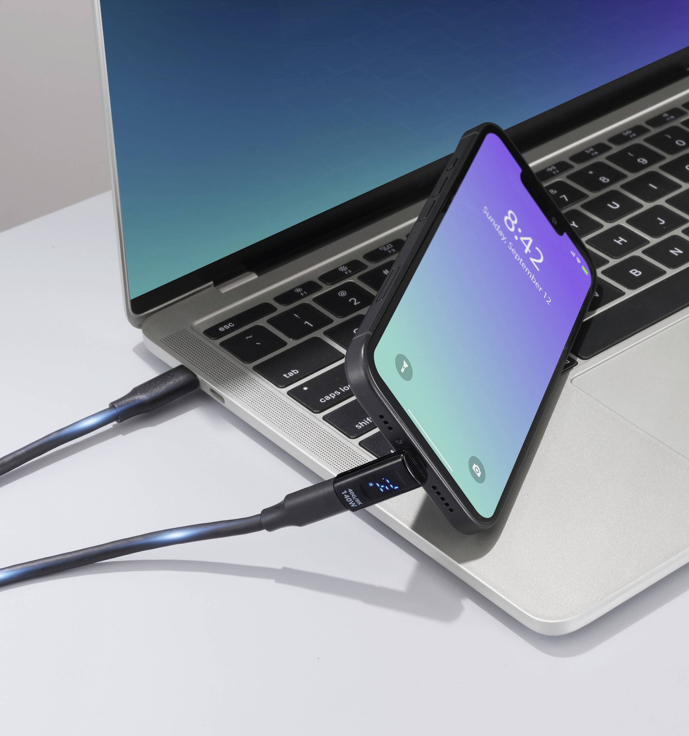 Smartphone připojený k notebooku nabíjecím kabelem zobrazuje zamčenou obrazovku s časem 8:42, což naznačuje, že je telefon připojen k nabíjení.
