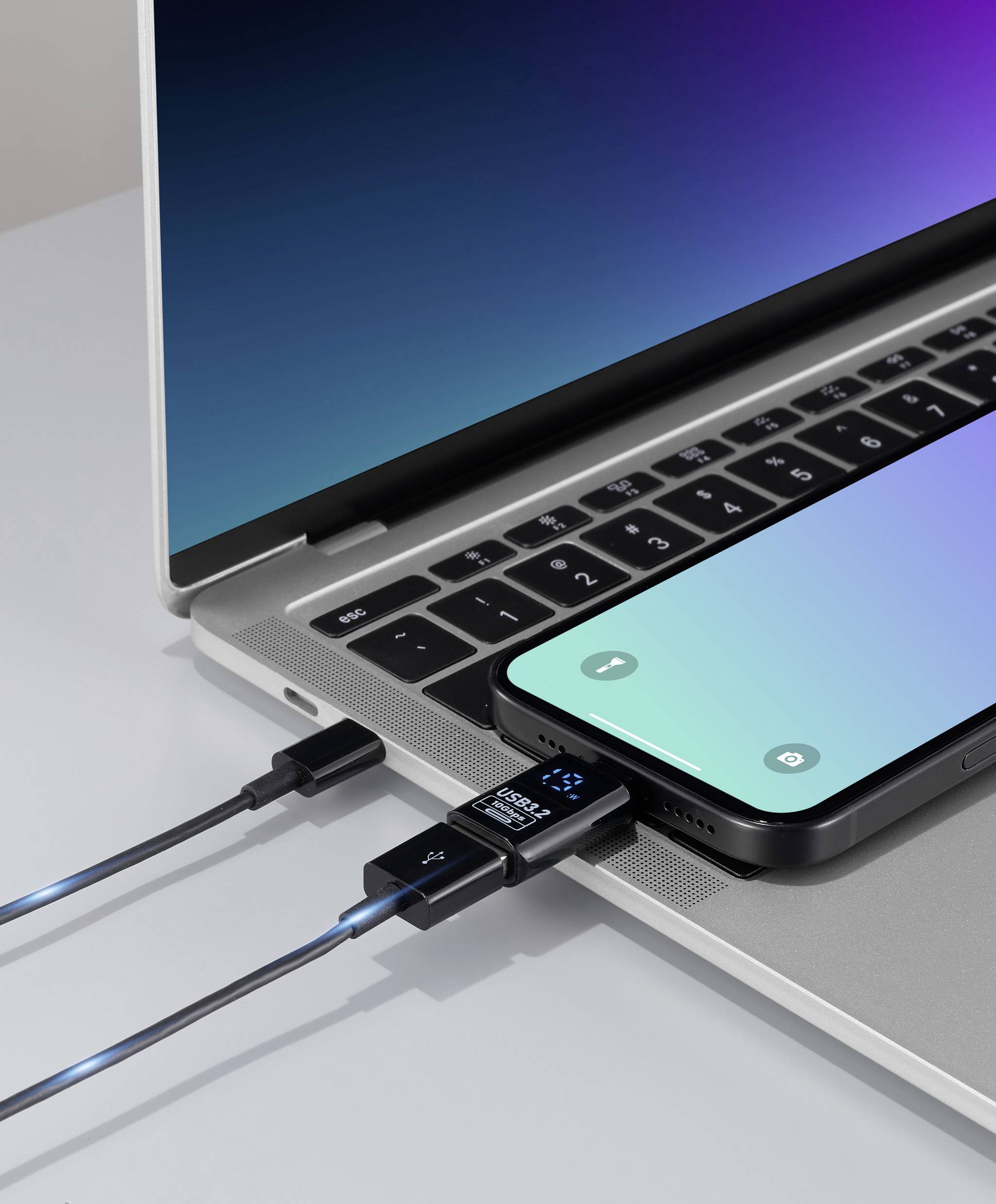 Smartphone připojený k notebooku pomocí USB kabelu, s digitálním měřičem zobrazujícím nabíjecí proud, který signalizuje přenos dat.
