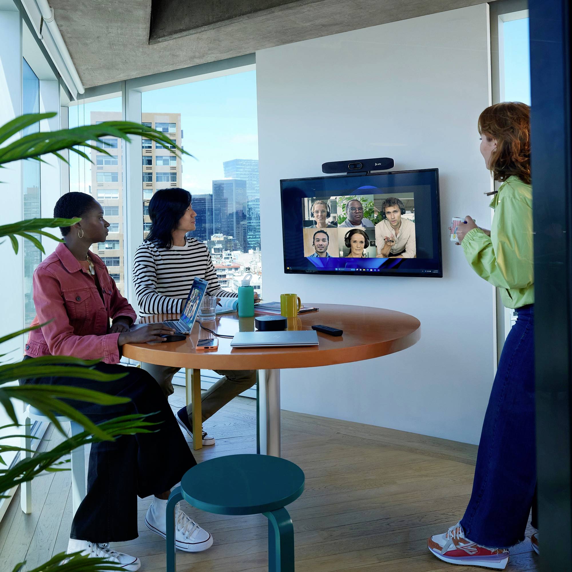 Čtyři osoby se setkávají virtuálně v moderní, světlé kanceláři. Na obrazovce je zobrazena videokonference s šesti účastníky.