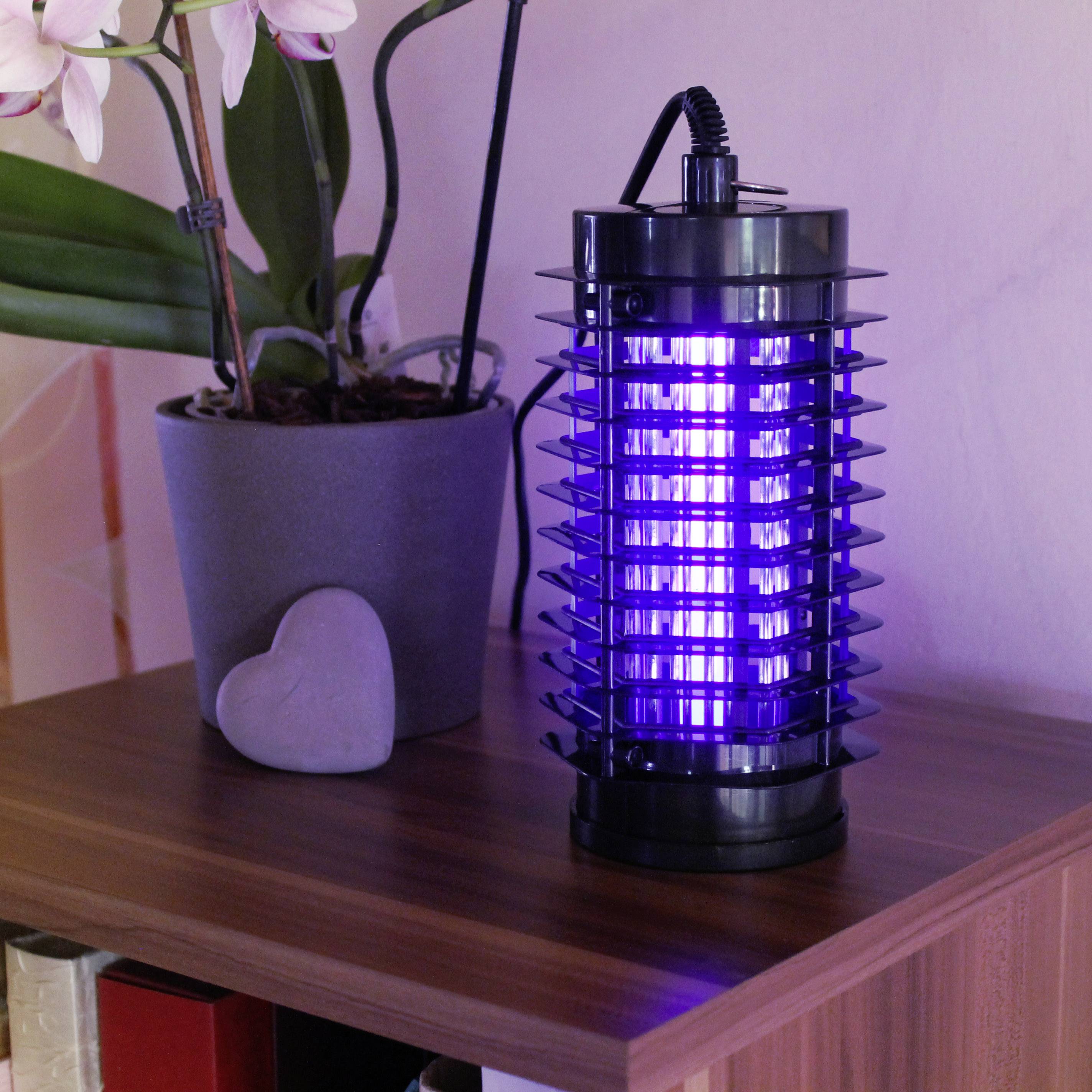 Elektrický lapač hmyzu na dřevěné polici vedle rostliny v šedém květináči. Lapač svítí modře.