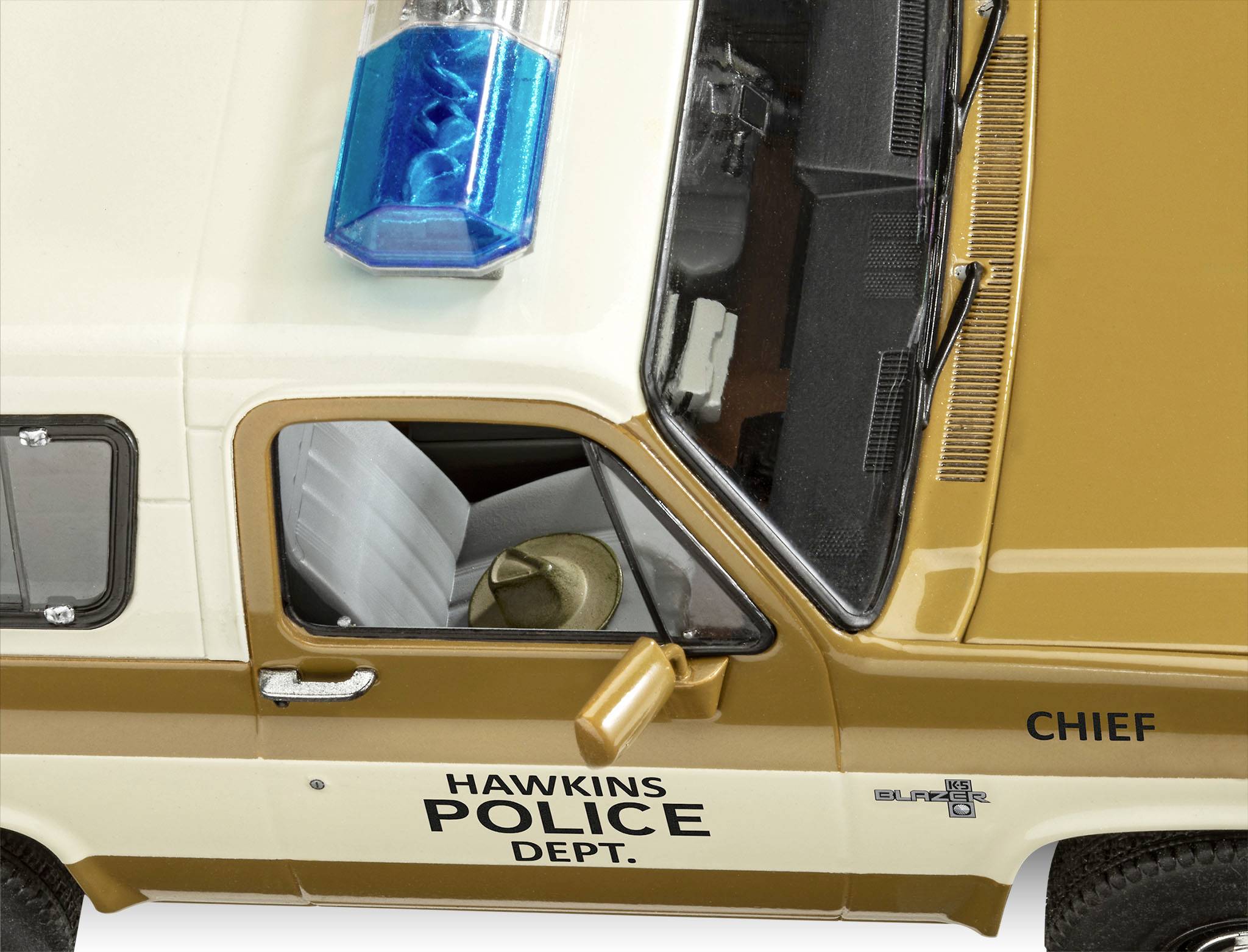 Krémové policejní vozidlo s nápisem 'Hawkins Police Dept.' a 'Chief' na dveřích. Je viditelný modrý světelný maják.