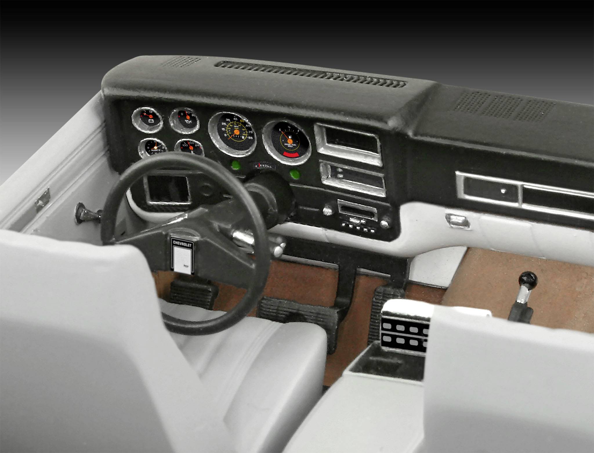 Interiér klasického automobilu s tmavou přístrojovou deskou, analogovými kruhovými přístroji, volantem a sedadly v bílo-šedém provedení.