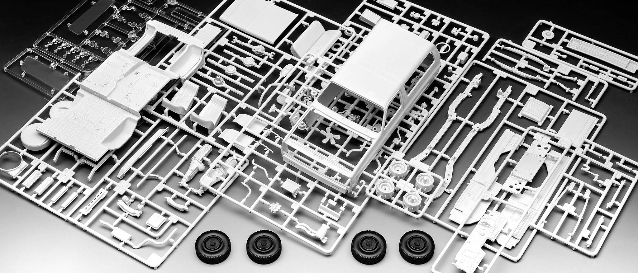 Plastový modelářský set s díly pro automobil, včetně karoserie, kol a různých drobných součástek, připravený k montáži.