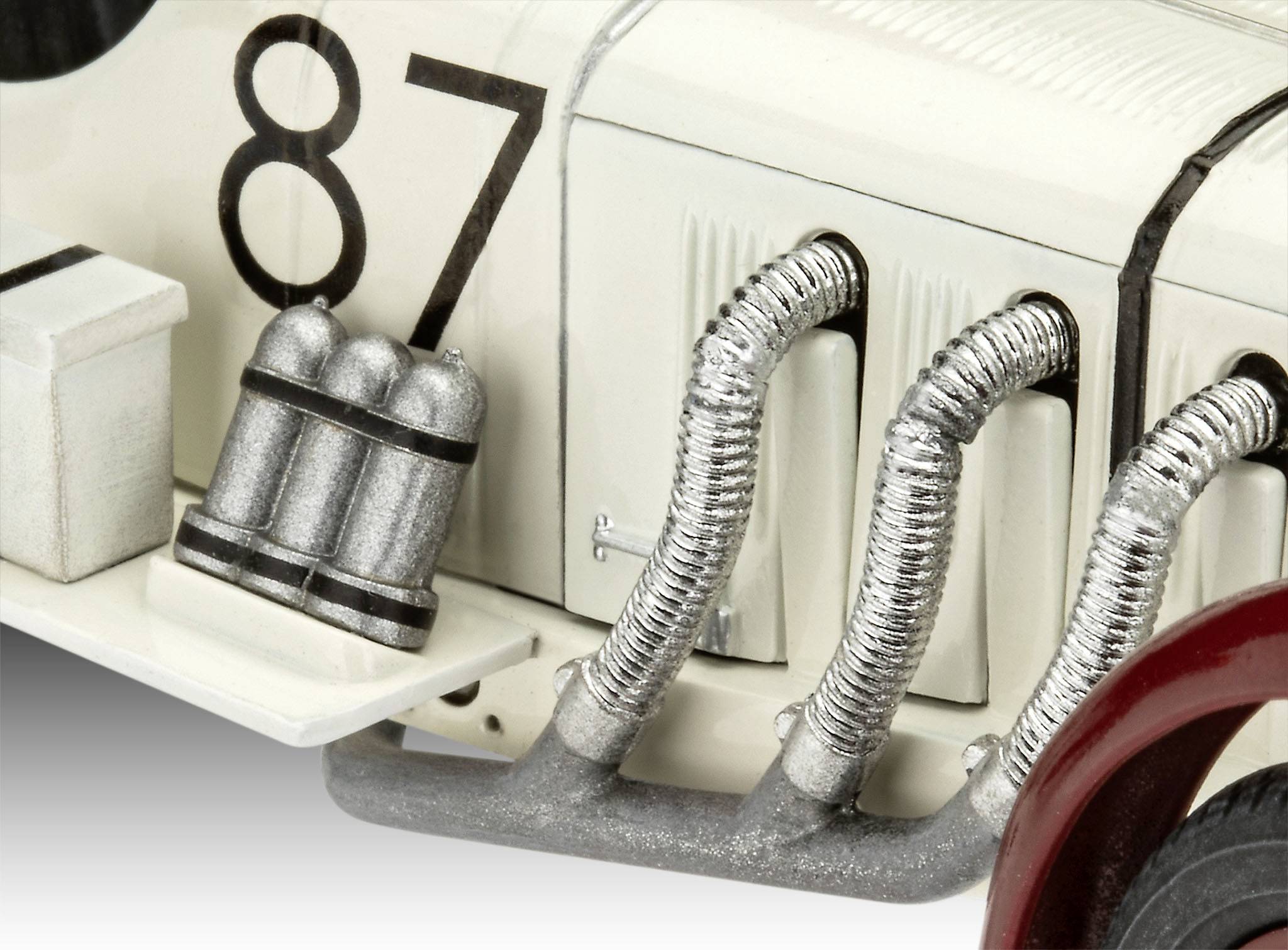 Model auta motor, bílý s číslem '87' a stříbrnými vedením, zobrazuje detailní části klasického automobilu.