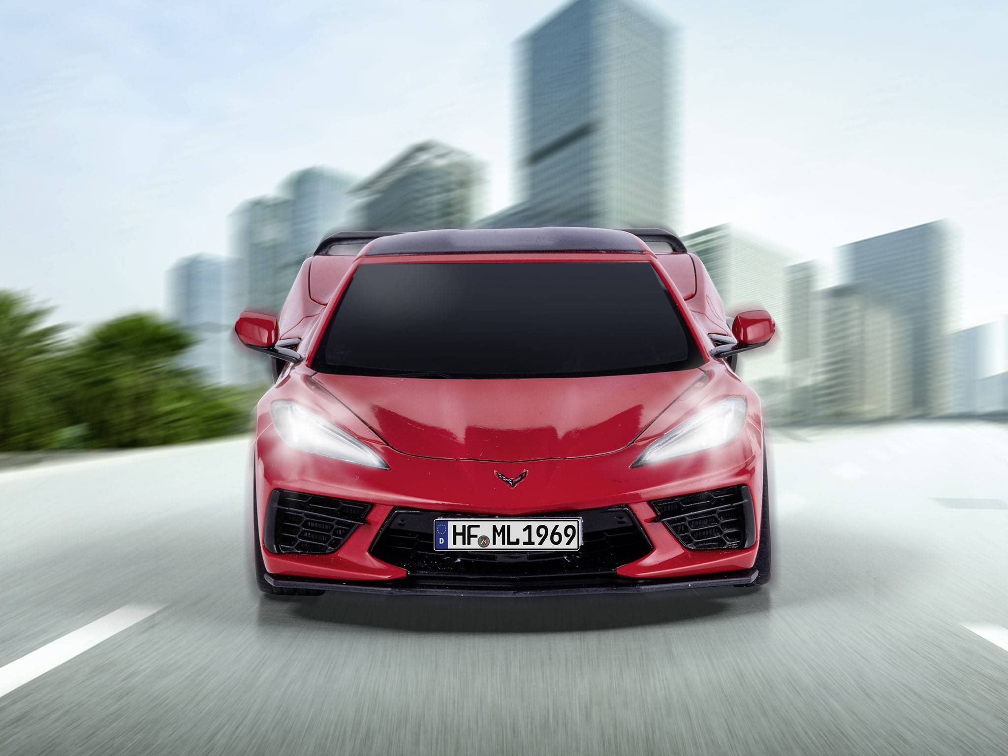 Červené sportovní auto jede po prázdné silnici před panoramatem města. Pohyb navozuje pocit rychlosti a dynamiky.